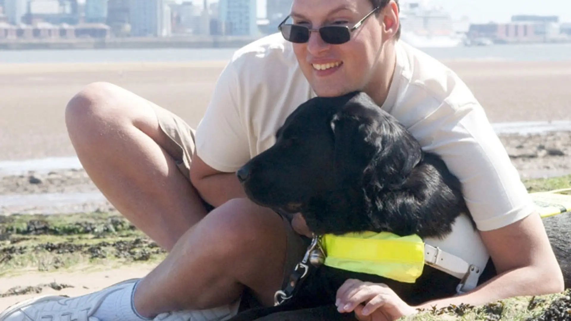 Guide Dog owner with guide dog sitting on the beach.