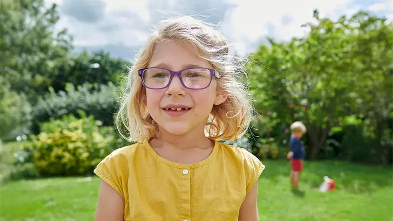 Josie smiles to camera, playing outdoors on a sunny day.