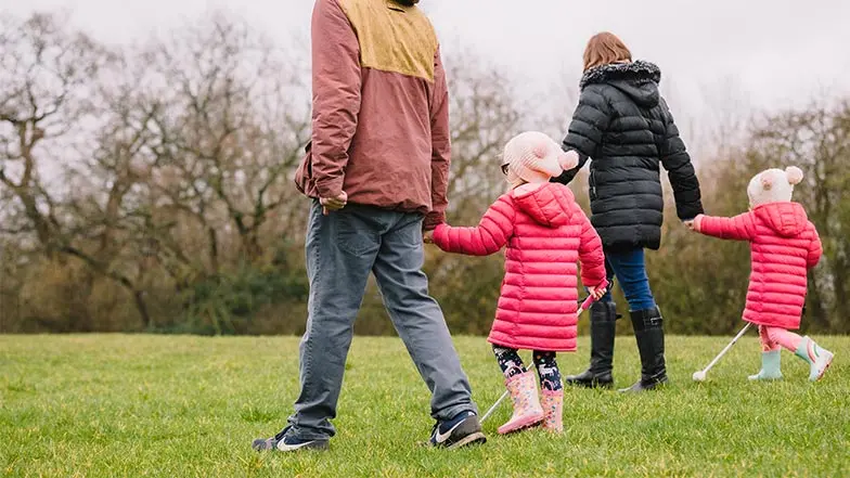 Alma and her sister Suzie, using their white canes, out walking with their parents
