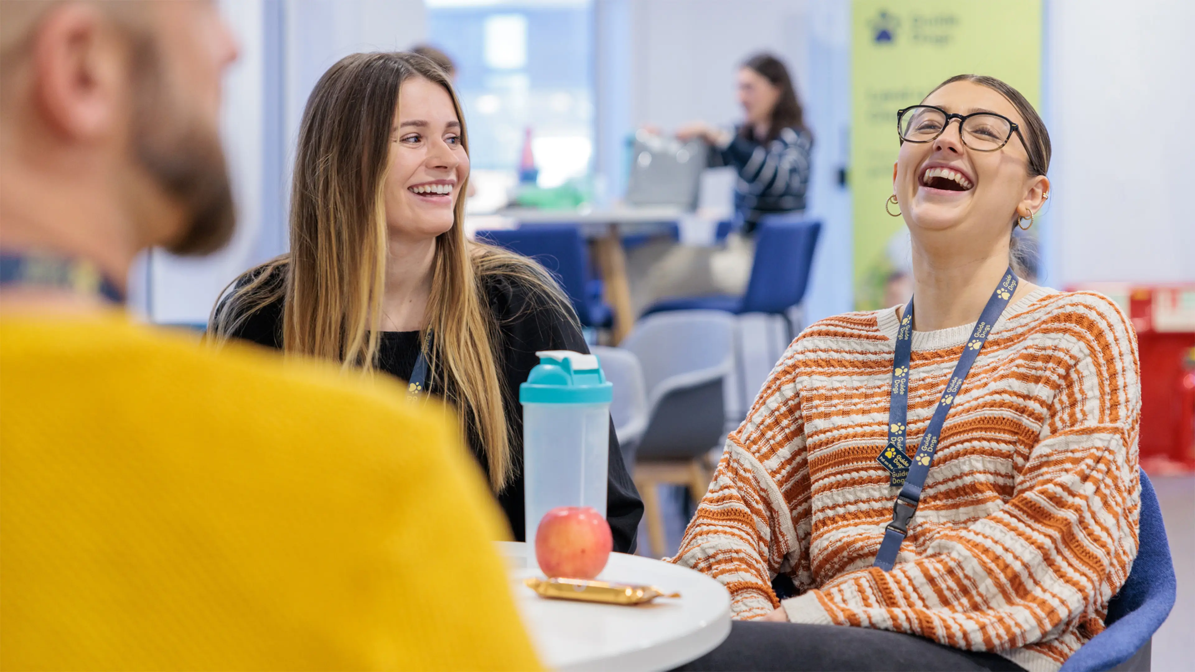 A Guide Dogs staff member throws back her head and laughs alongside two of her colleagues at lunch.