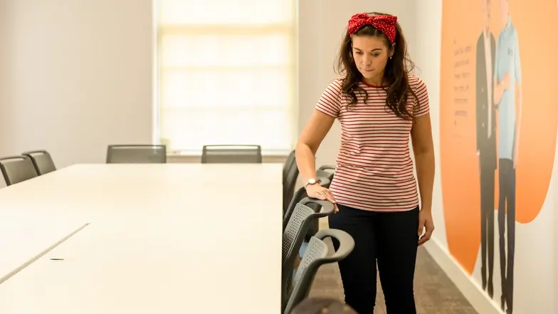 A woman runs her hand across the top of the chairs in a room to familiarise herself with the space.