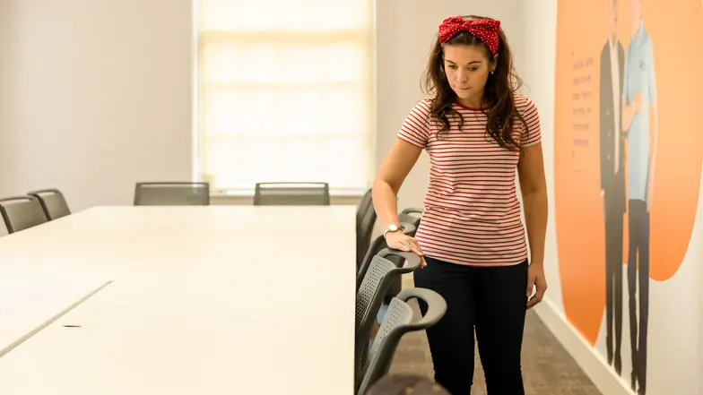 A woman runs her hand across the top of the chairs in a room to familiarise herself with the space.