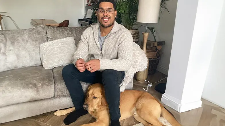 Devante and guide dog Mack sit in their living room.