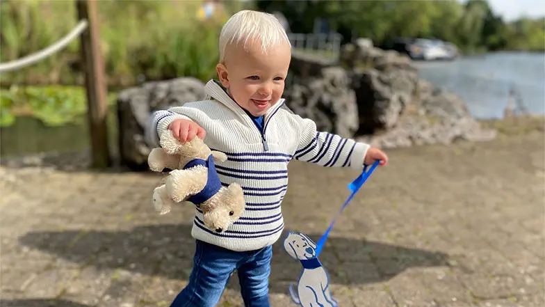 A young child outside on a walk holding a Guide Dogs cuddly toy and cut out of a guide dog
