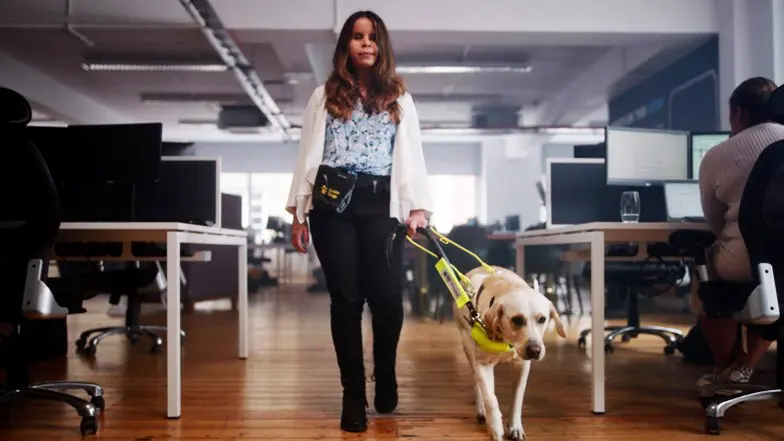 A young woman walking with her guide dog through an office.