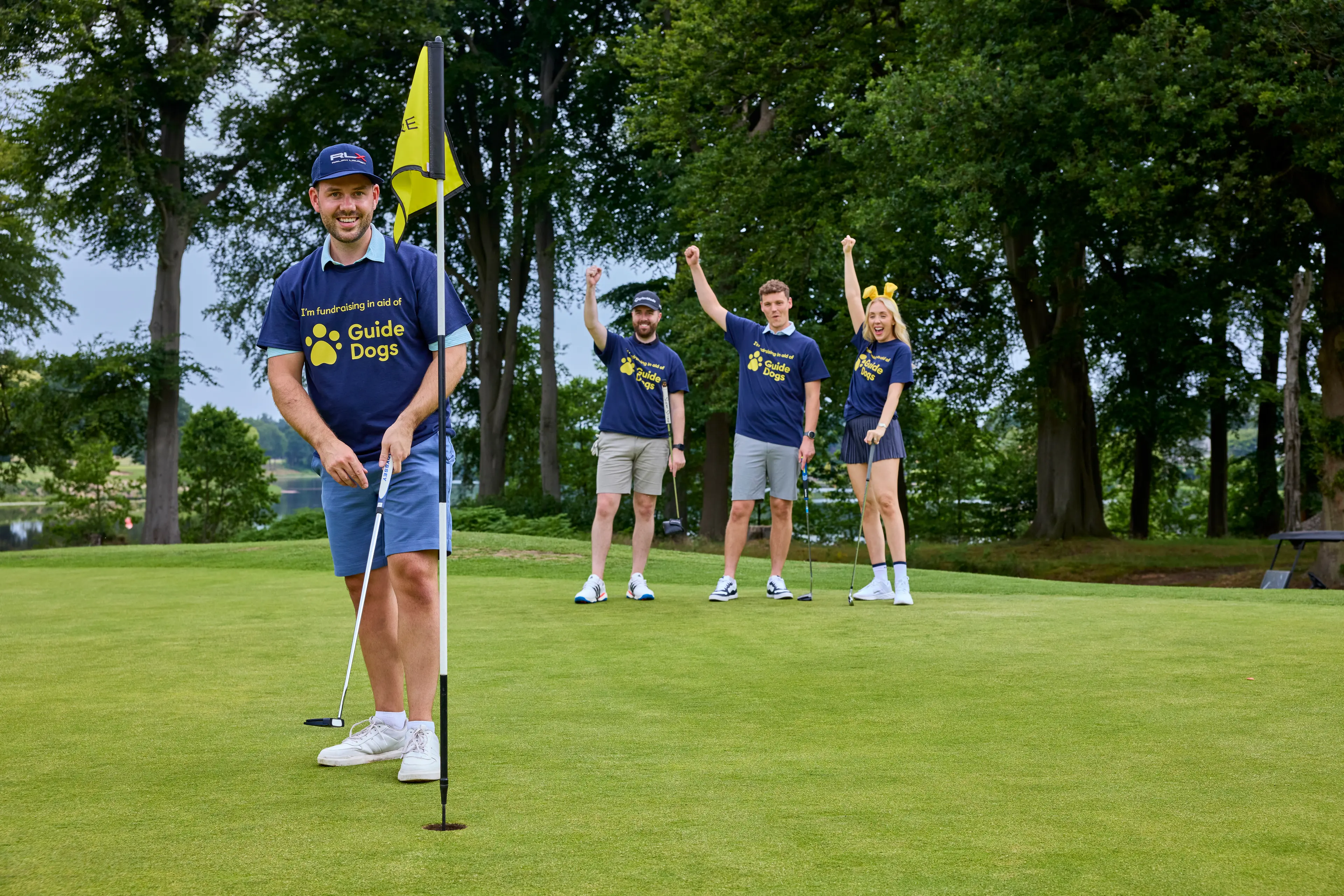 A woman and three men play golf wearing Guide Dogs tshirts.