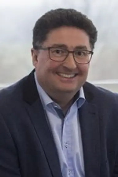 Mike is smiling at the camera. He has short dark hair, wears glasses, and is wearing a dark suit.