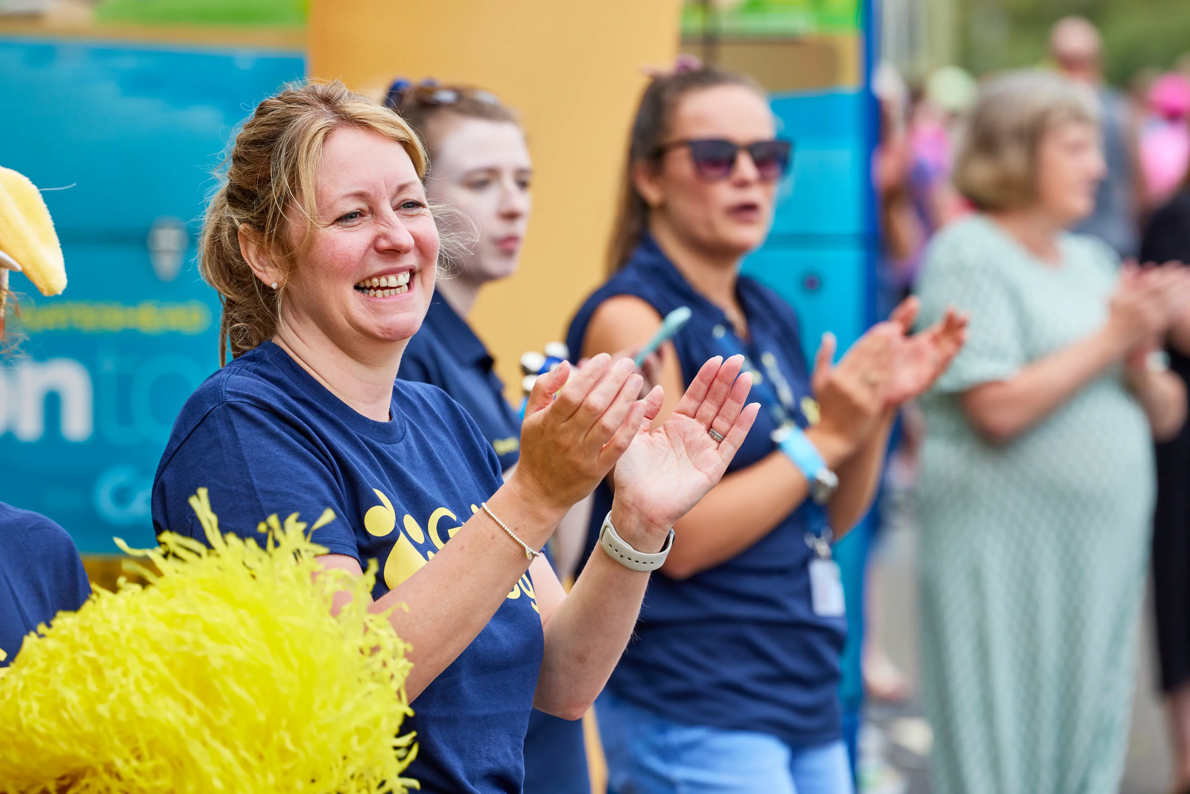 Three women wearing Guide Dogs t-shirts are in the crowd cheering at a race.