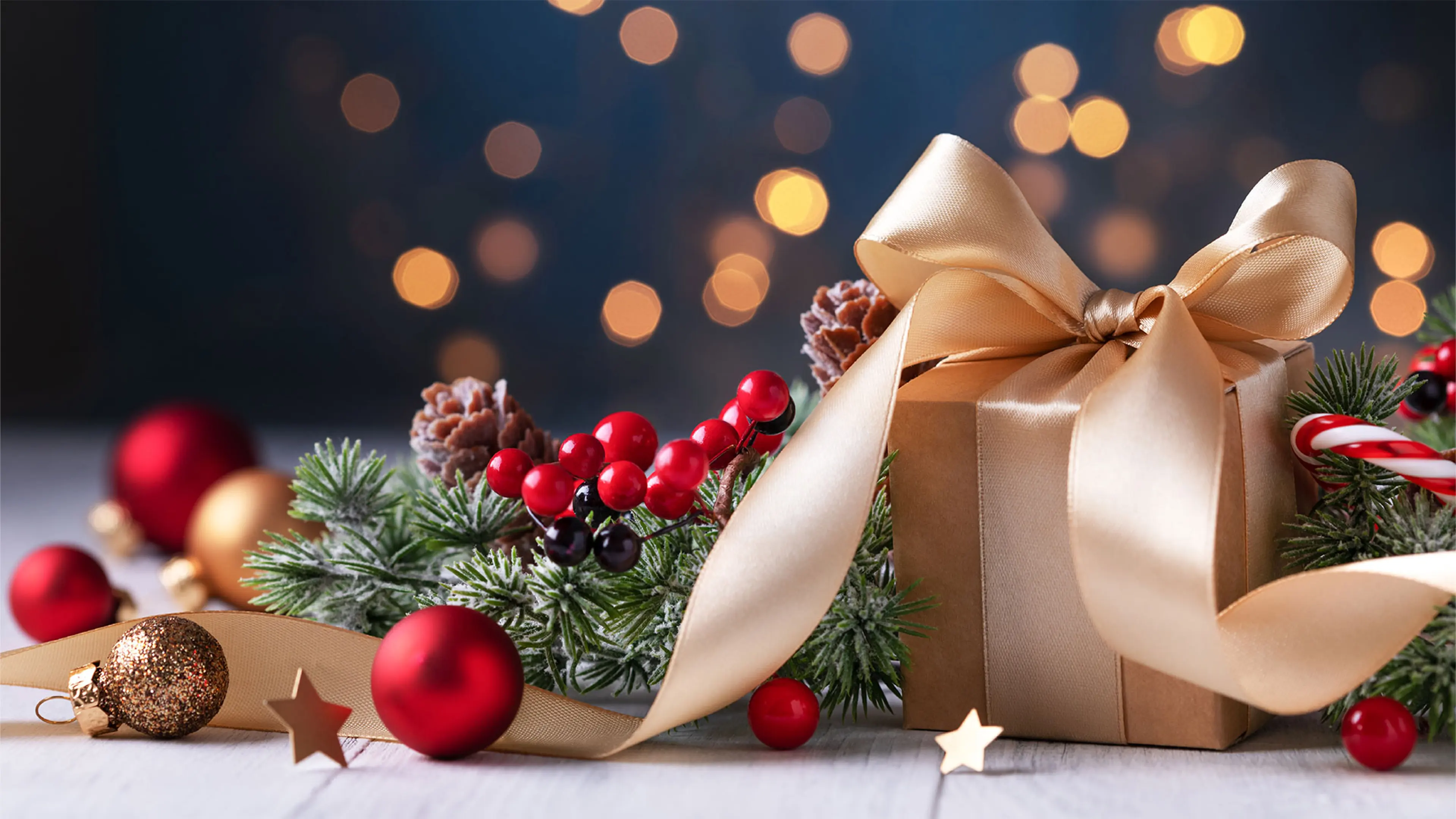 Beautifully wrapped Christmas gift and Christmas wreath, lights sparkle in the background.
