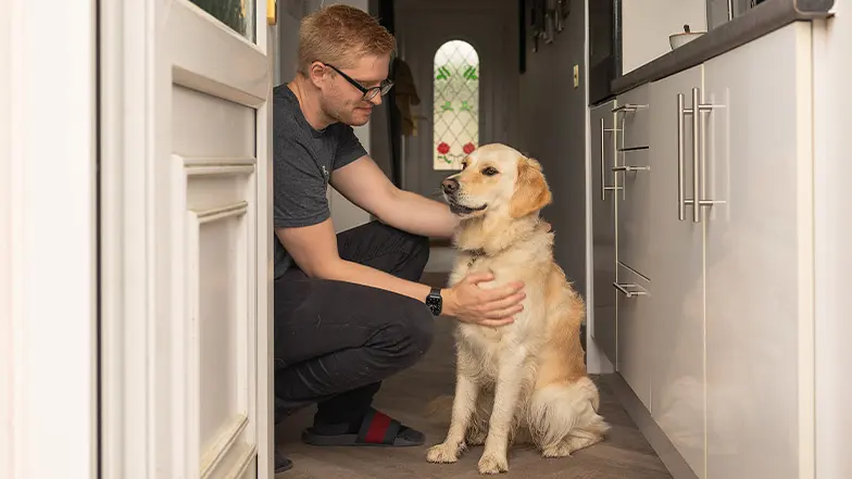 A dog owner strokes his dog as they sit on the floor of their home.