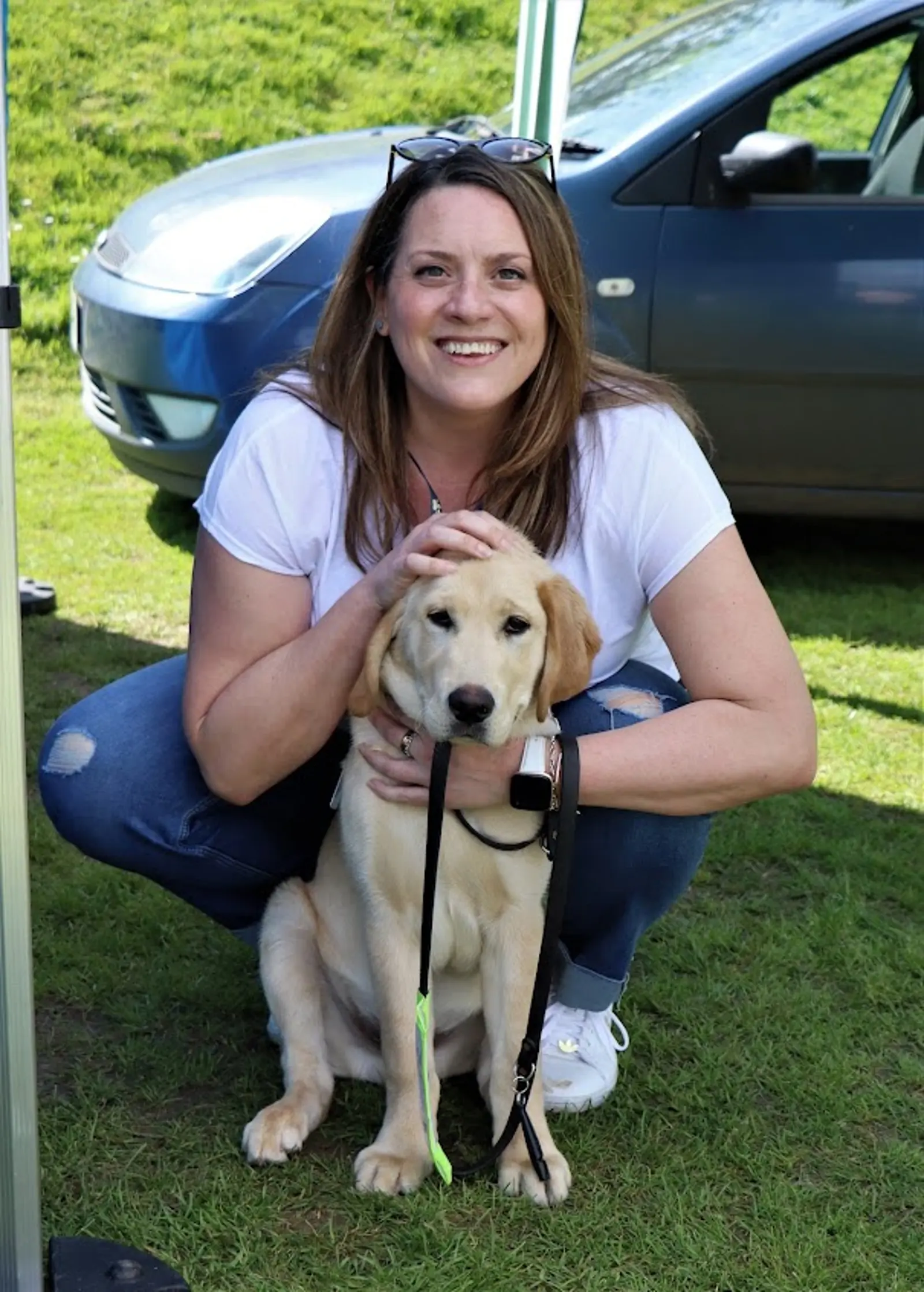 Tracey Berridge, Head of Volunteering crouches down with a guide dog puppy Cosmo sat in front of her