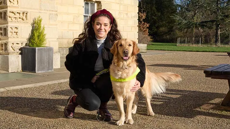 Taylor, and her guide dog, Jilly, smile as they sit together.