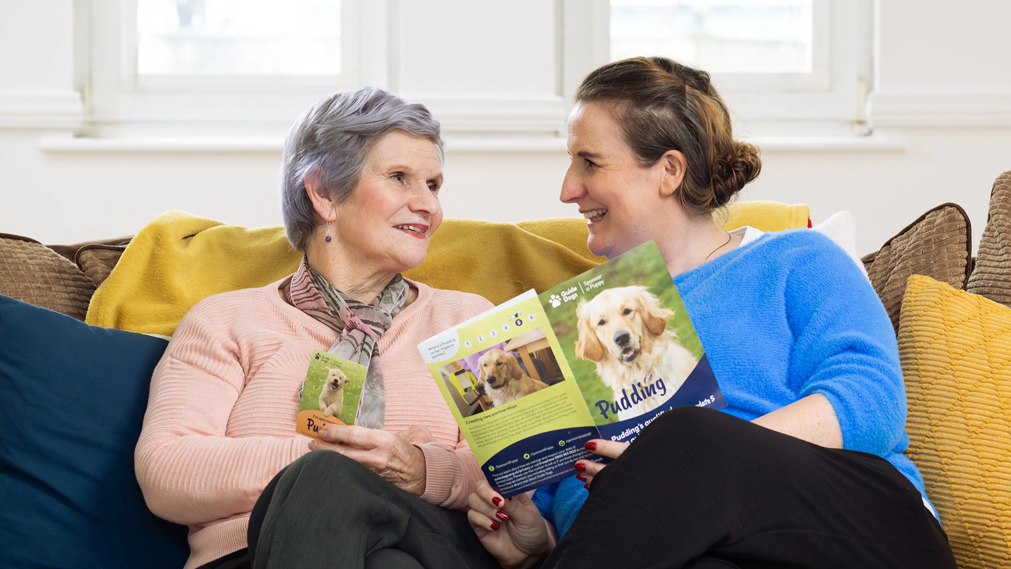 Michelle and her mum sit together on a sofa. Michelle is holding a Pudding printed Pupdate whilst her mum holds a Pudding fridge magnet.