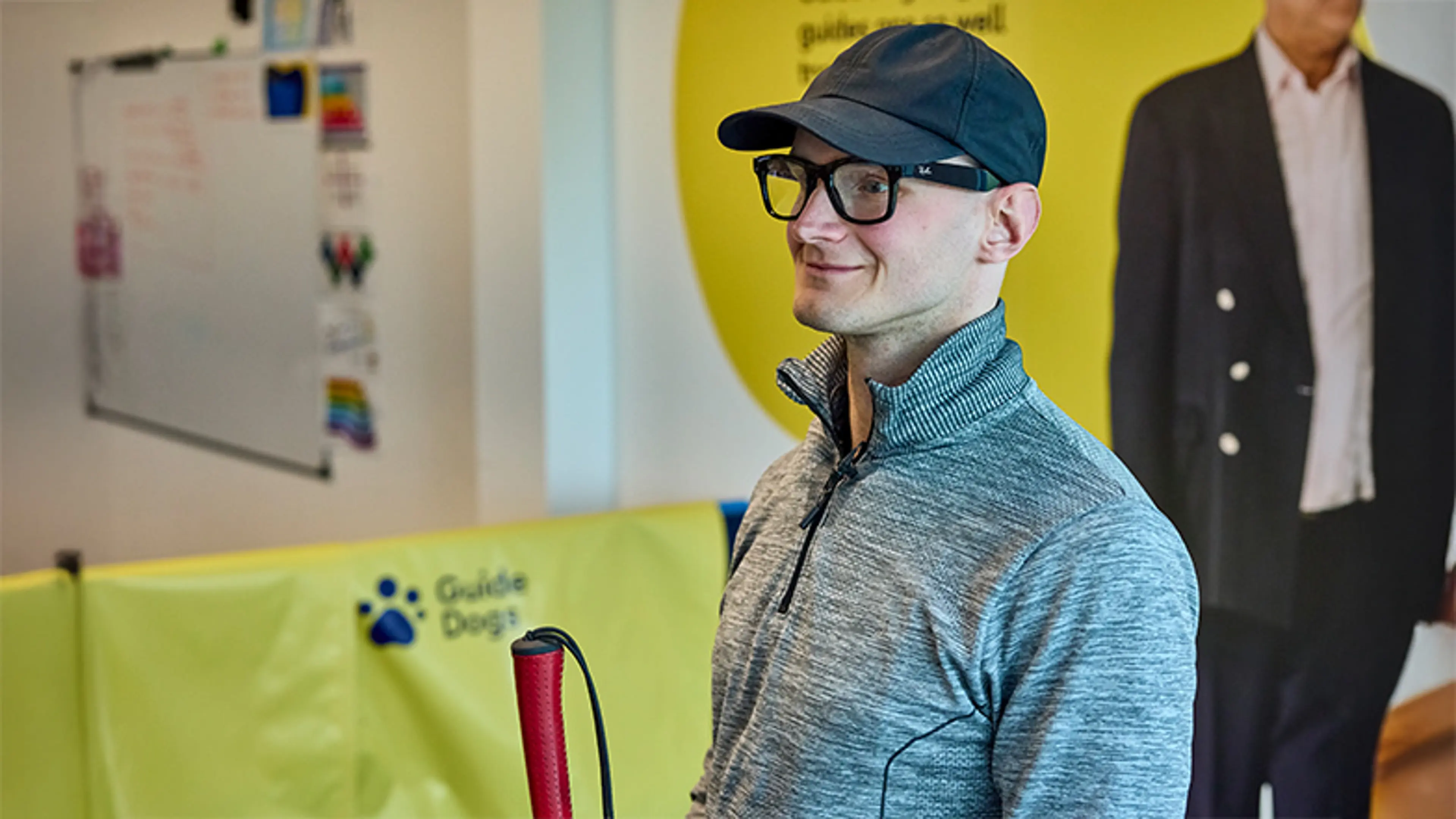 Tech user Peter uses his Ray-Ban smart glasses and a long cane to navigate the Guide Dogs office.