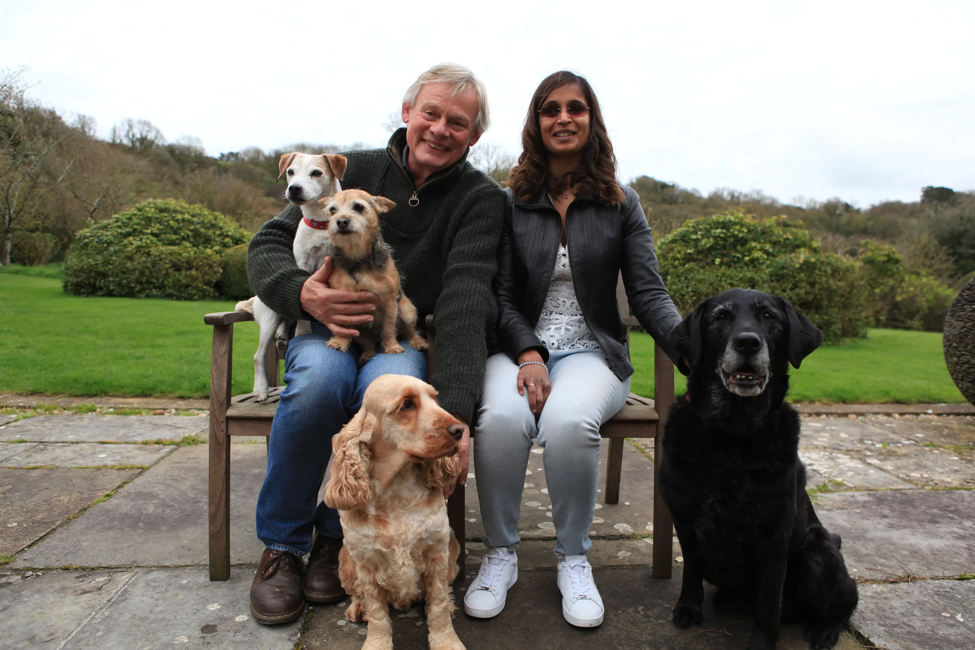 Jaina and Martin sit on a bench with Martin's dogs, including Jaina's retired guide dog Laura.
