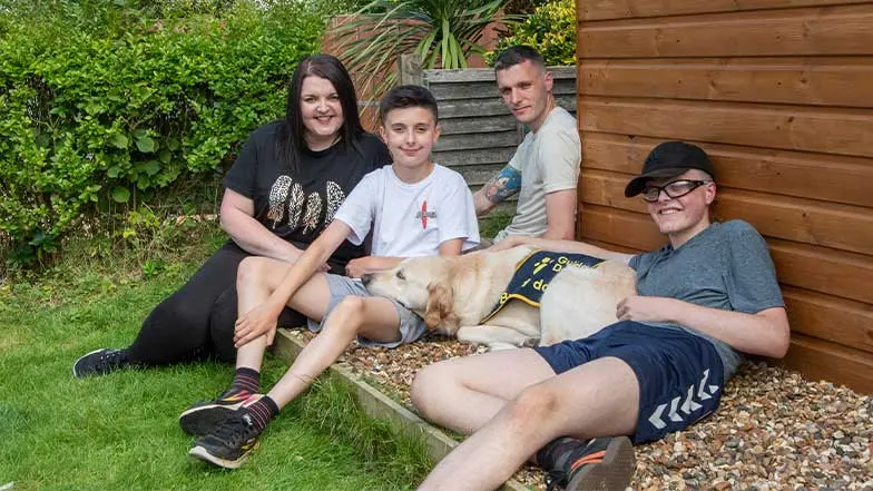 Declan, a young service user, and his family, sit in the garden with Declan's buddy dog.