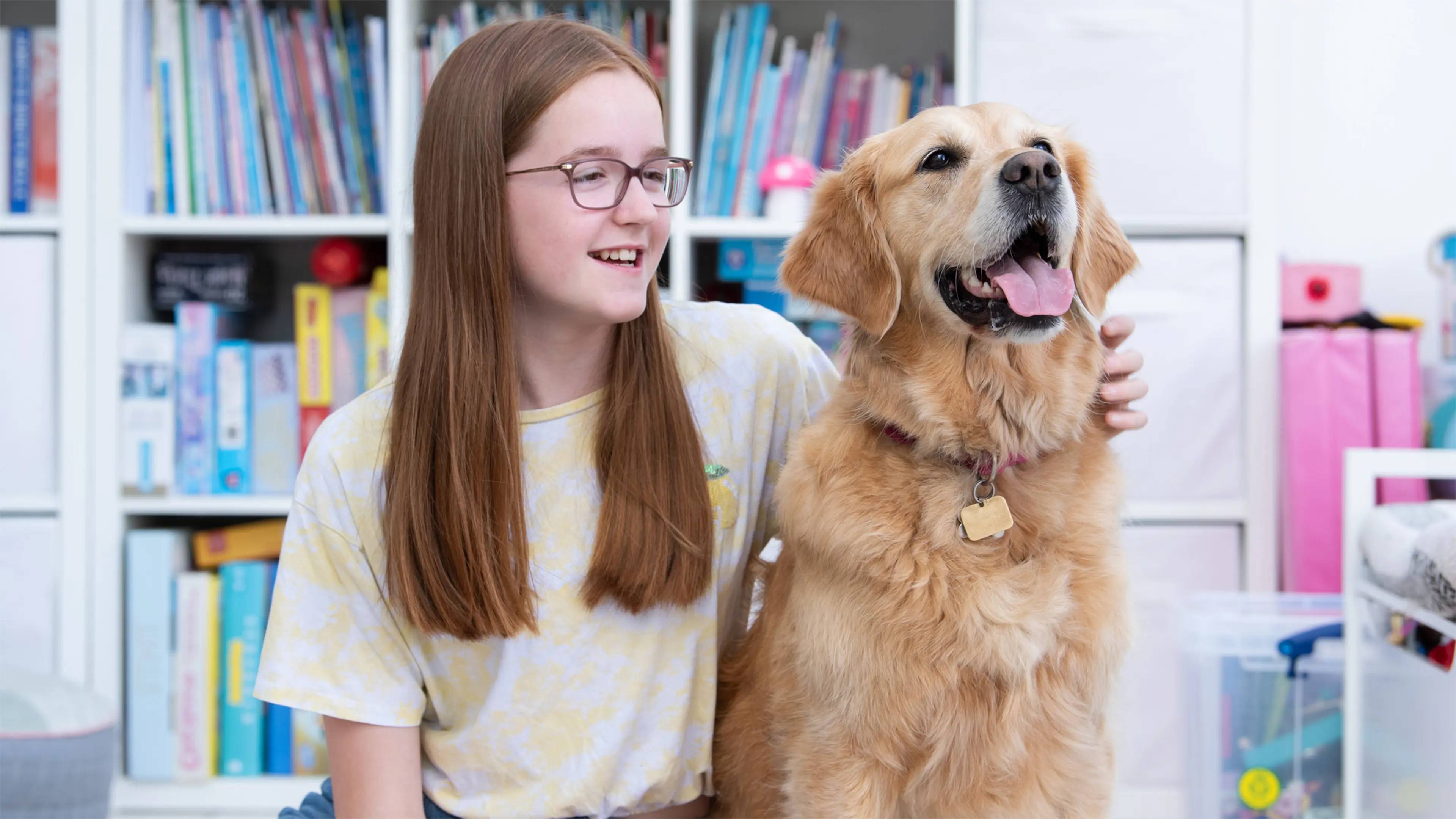Freya, who has a vision impairment, sits in her house with her arm around her buddy dog, golden retriever Gwen.