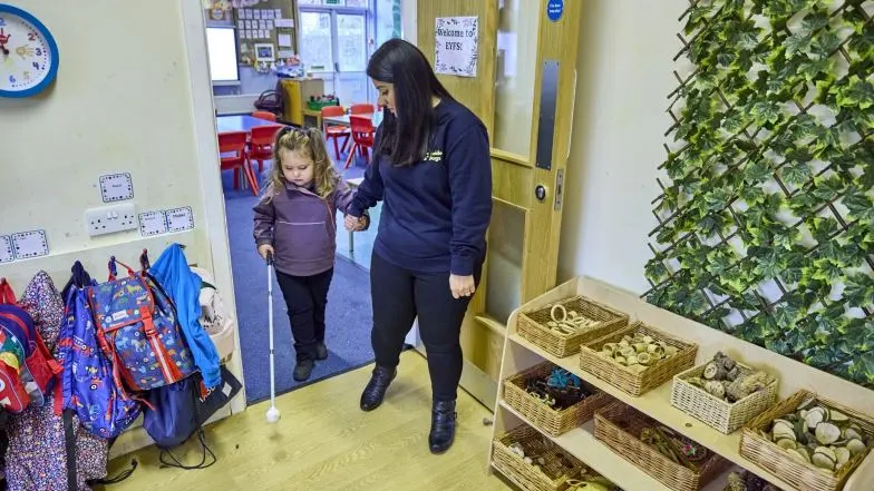 Habilitation specialist Sunita helps a young girl with a vision impairment use a white cane to navigate through a school.