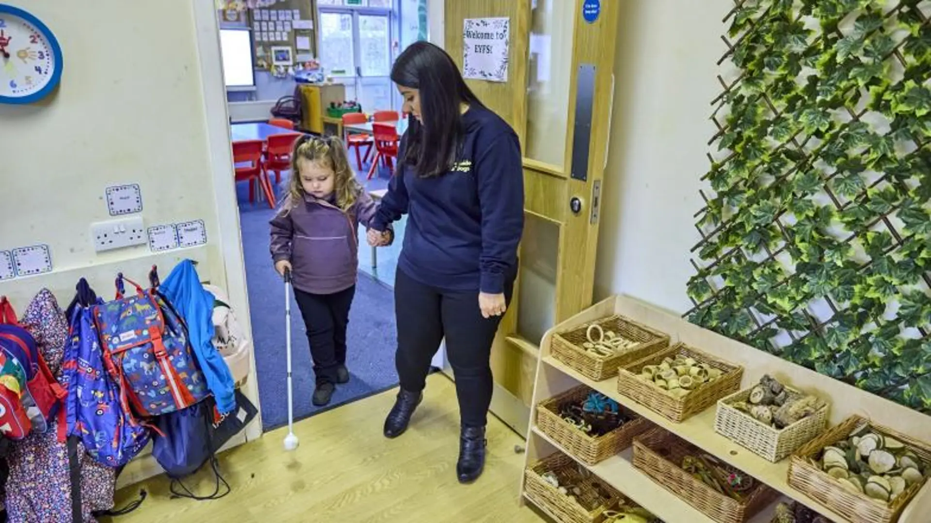Habilitation specialist Sunita helps a young girl with a vision impairment use a white cane to navigate through a school.