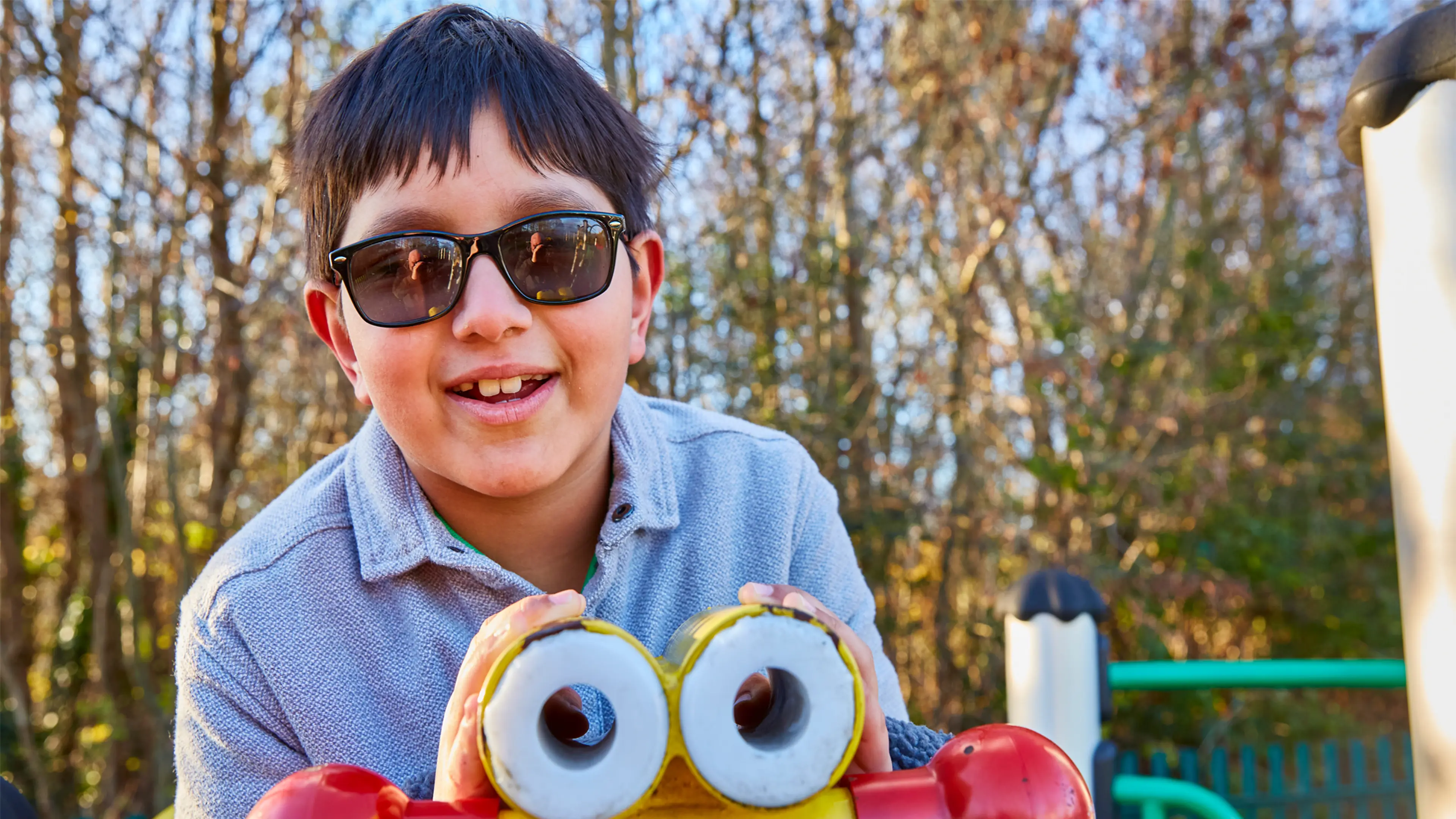 Teddy, a child who has a vision impairment, sits smiling as he plays on a piece of equipment in a playground.