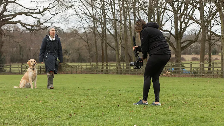 A Video Producer filming a rehomer and her dog in their garden.