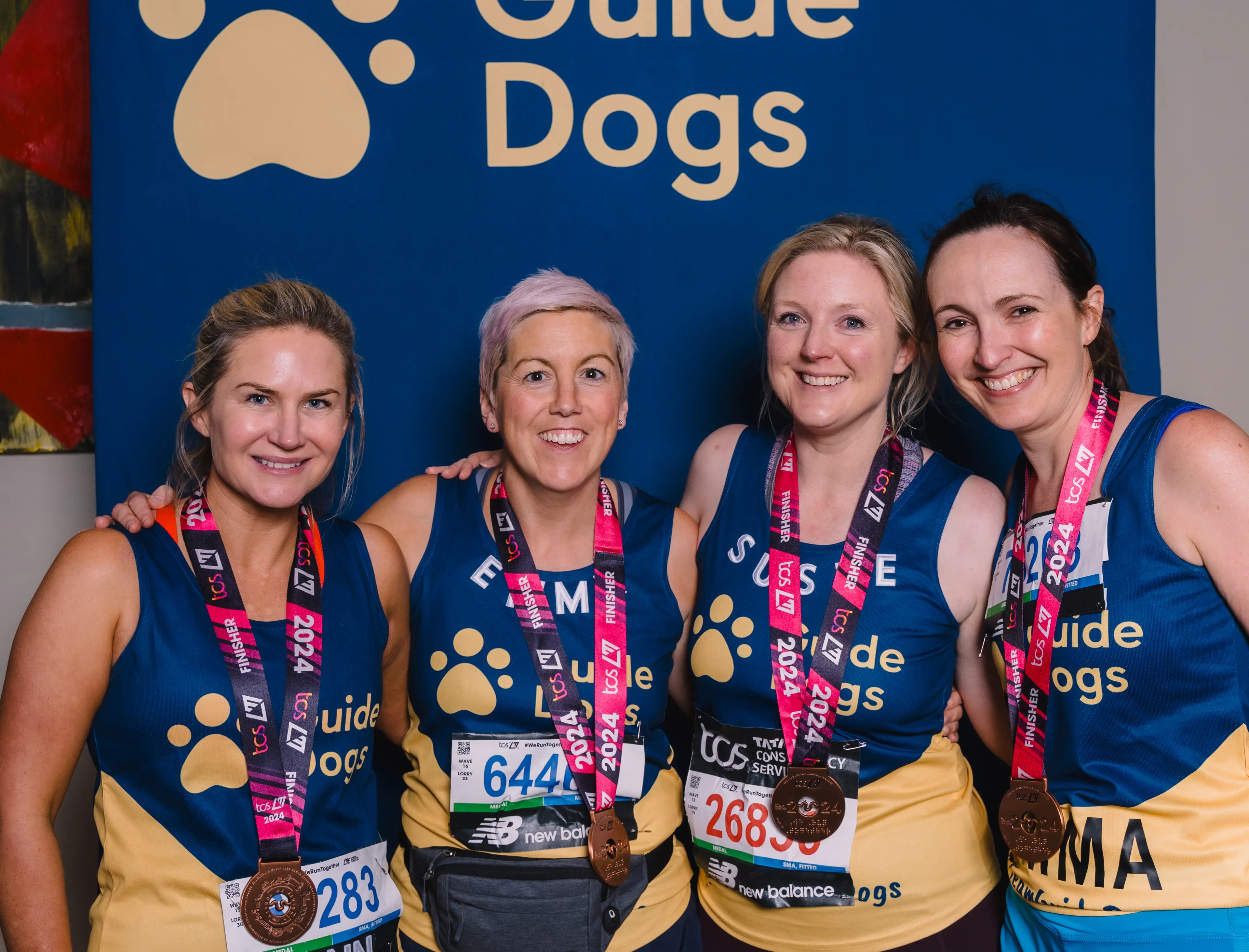 Four Guide Dogs London Marathon runners wearing medals smiles.