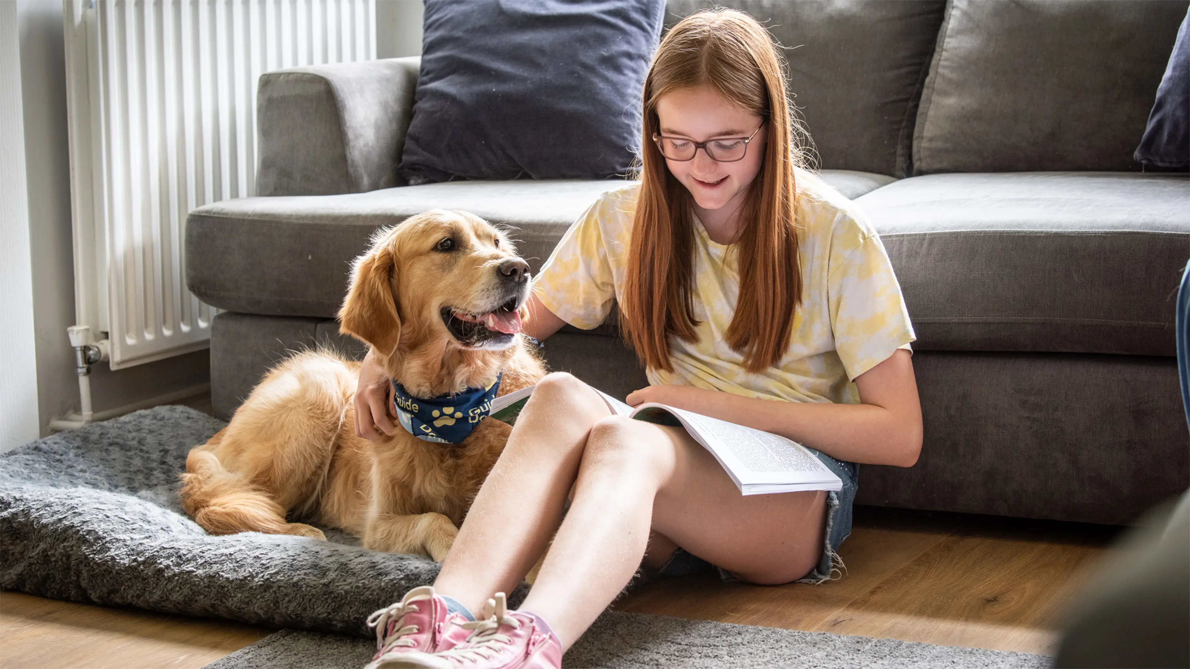 Freya, who has a vision impairment, sits on the floor reading a book beside her buddy dog Gwen, a golden retriever. 
