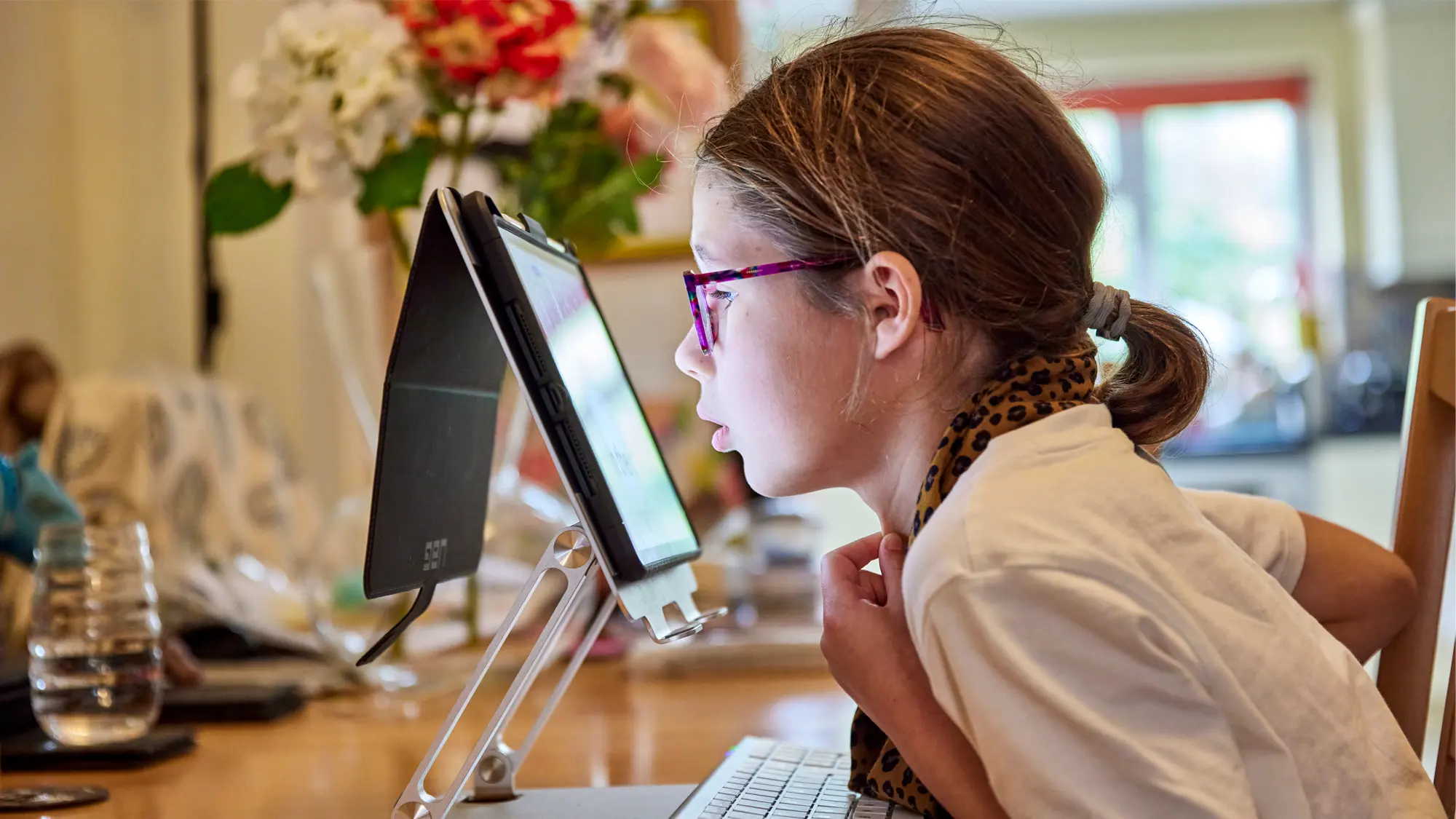 Erin, a young girl with vision impairment, sits at her kitchen table and uses an iPad with assistive technology features.