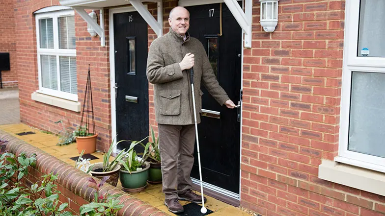 Guide Dogs' staff member at the front door of his home with his long cane