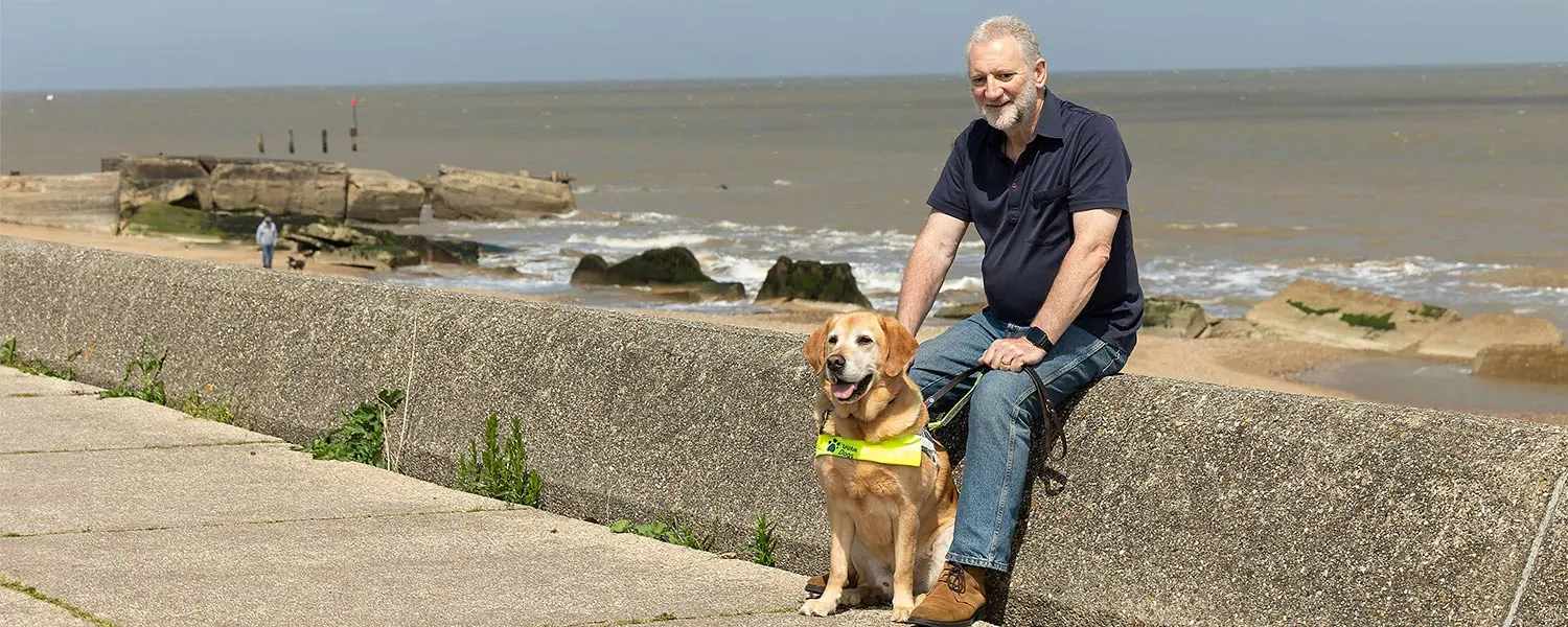 Guide dog owner Simon with guide dog Mayne sitting on a wall at the beach.