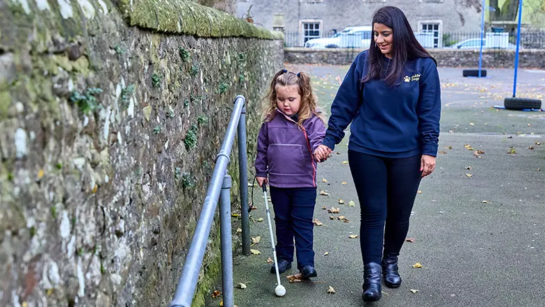 Sunita a habilitation specialist with a vision impairment, guiding four-year-old Mabel on how to use her cane.