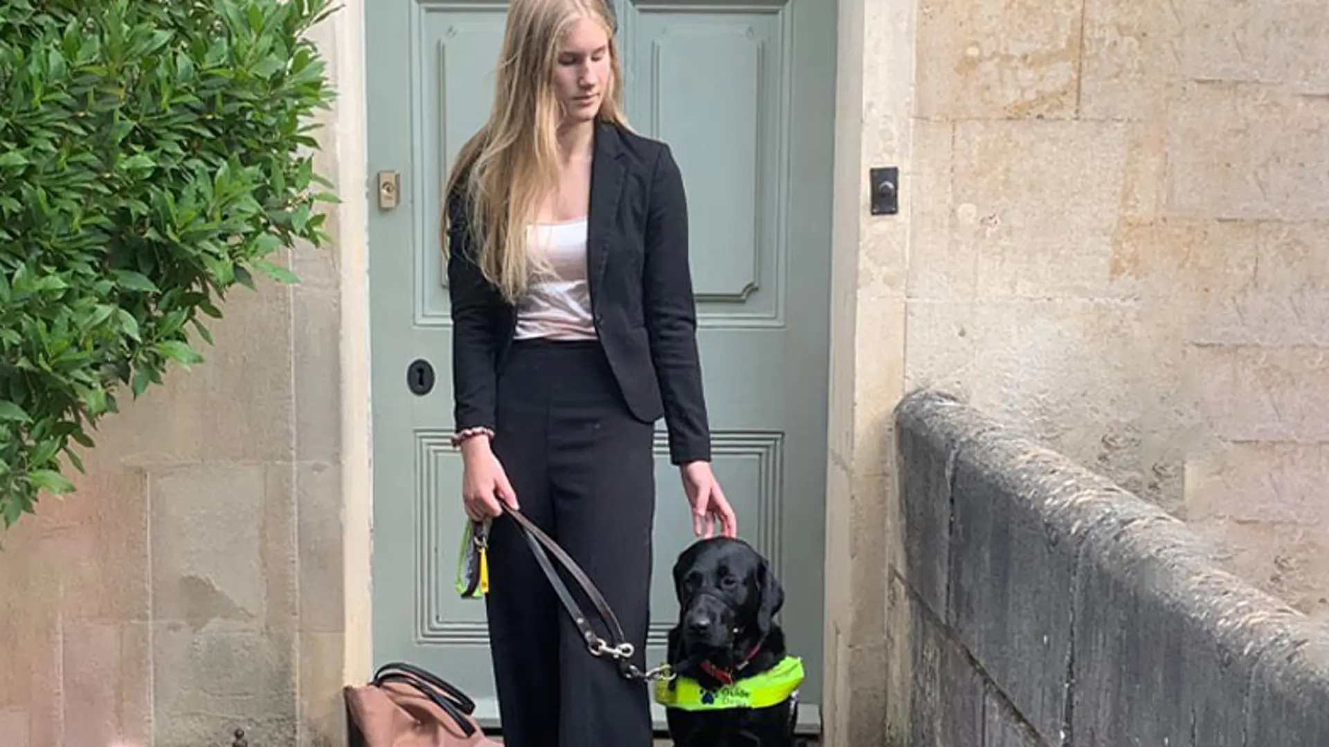 A guide dog owner and her guide dog stand in front of their home.