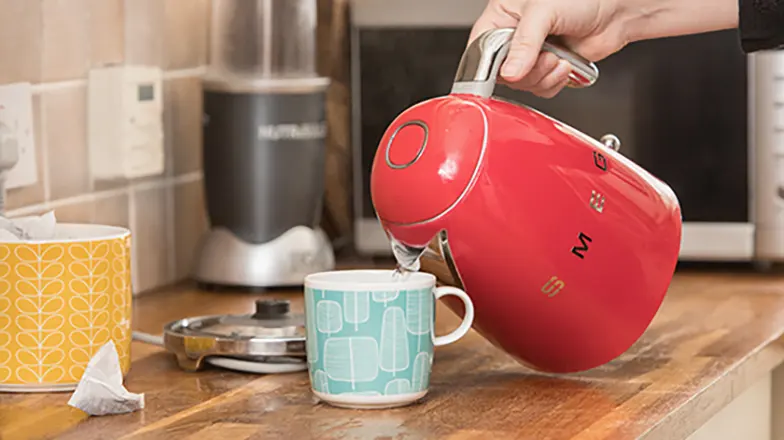 Person pouring hot water into mug from red kettle