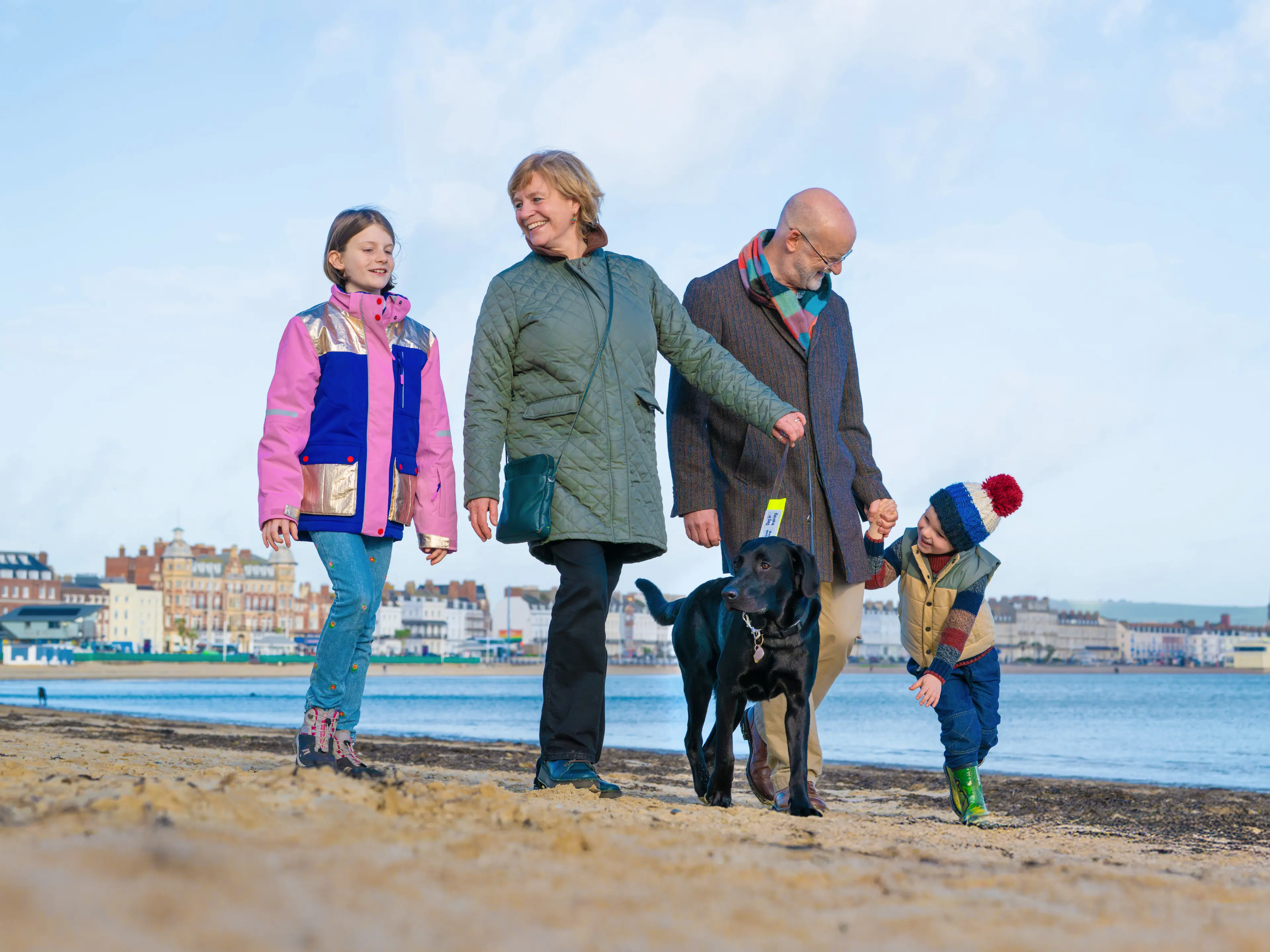 A family of volunteer puppy raisers walk with a guide dog puppy on a beachfront 