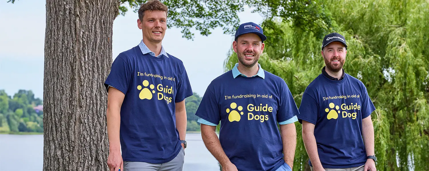 Three fundraisers wear guide dog t-shirts and smile outdoors