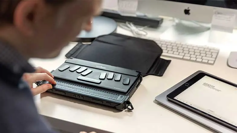 A man uses a humanware braille reader to read