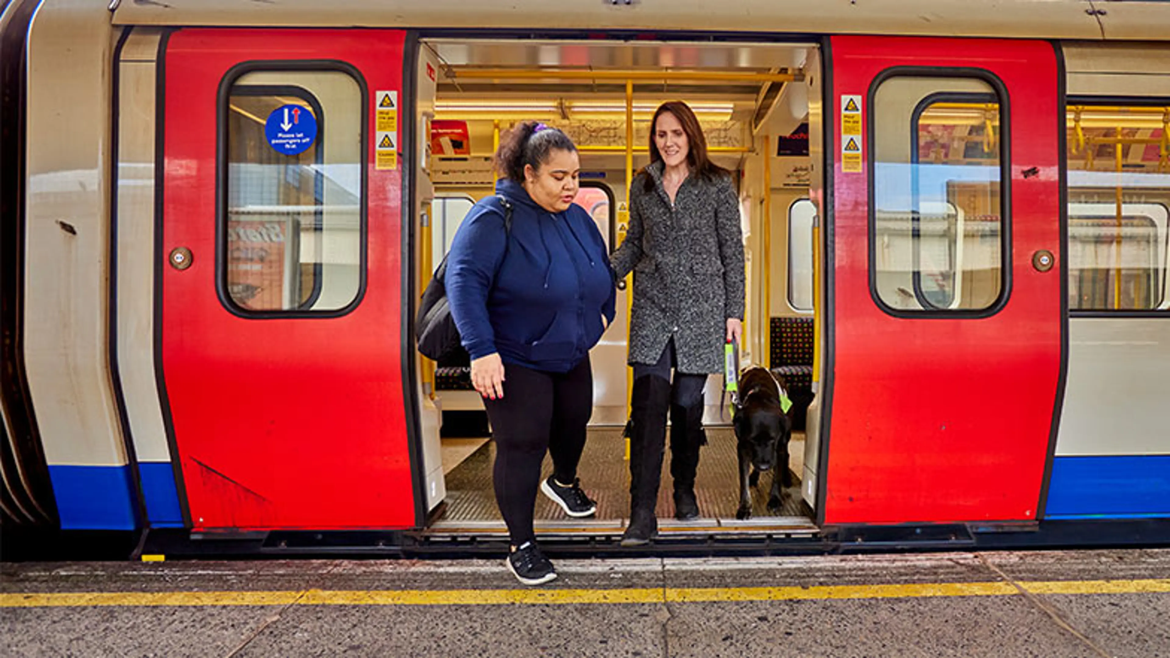 A guide dog owner being guided off a train